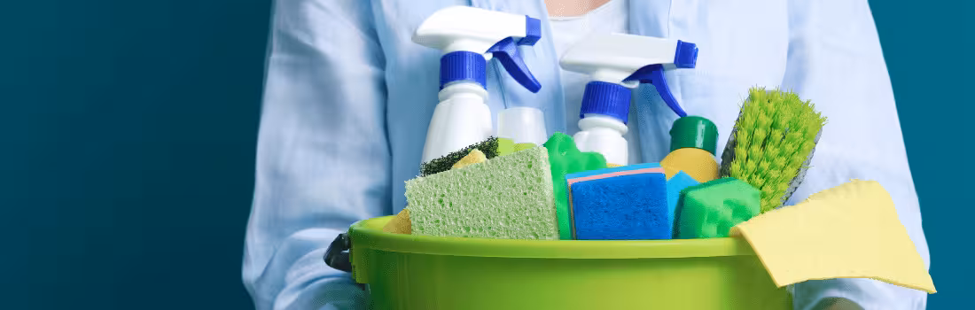 A person holding a bucket with different cleaning supplies and surface disinfectant