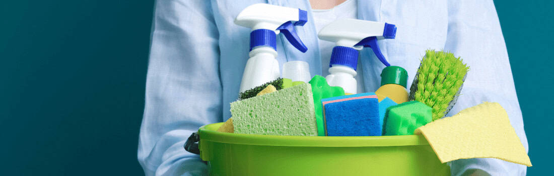 A person holding a bucket with different cleaning supplies and surface disinfectant