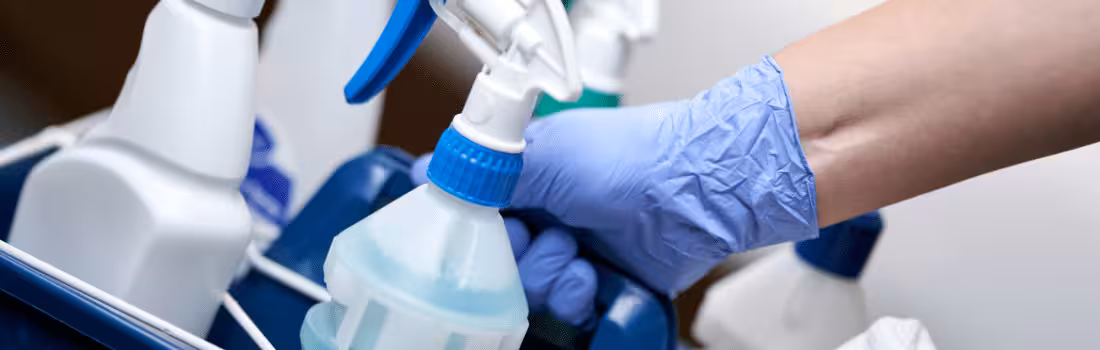 A gloved hand holding a bucket with different COVID-19 disinfectant