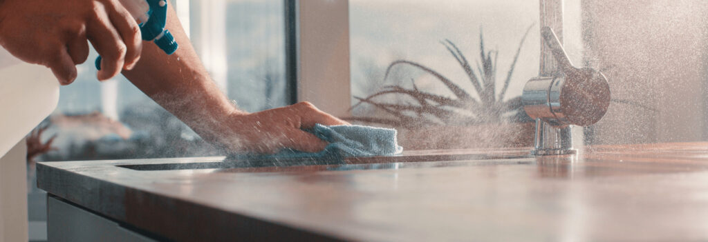 A person wiping down countertops with spray and a rag
