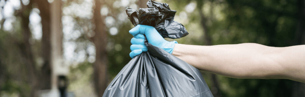 A person holding a trash bag that could benefit from an odor eliminator spray