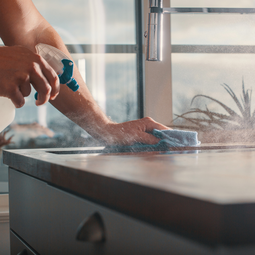 A person spraying and wiping down a countertop to disinfect the surface