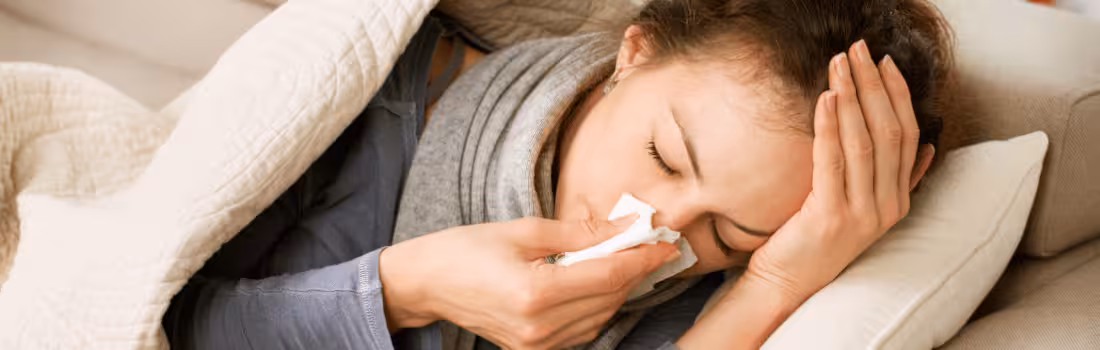 A woman suffering from cold and flu, lying down and holding a tissue to her nose